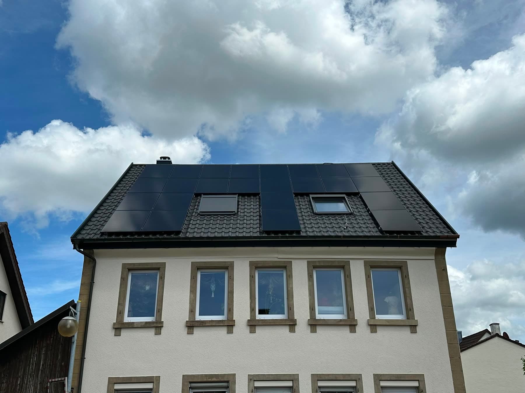 Fertiggestelltes Mehrfamilienhaus mit dunklem Dach, Solarmodulen und zwei Gauben